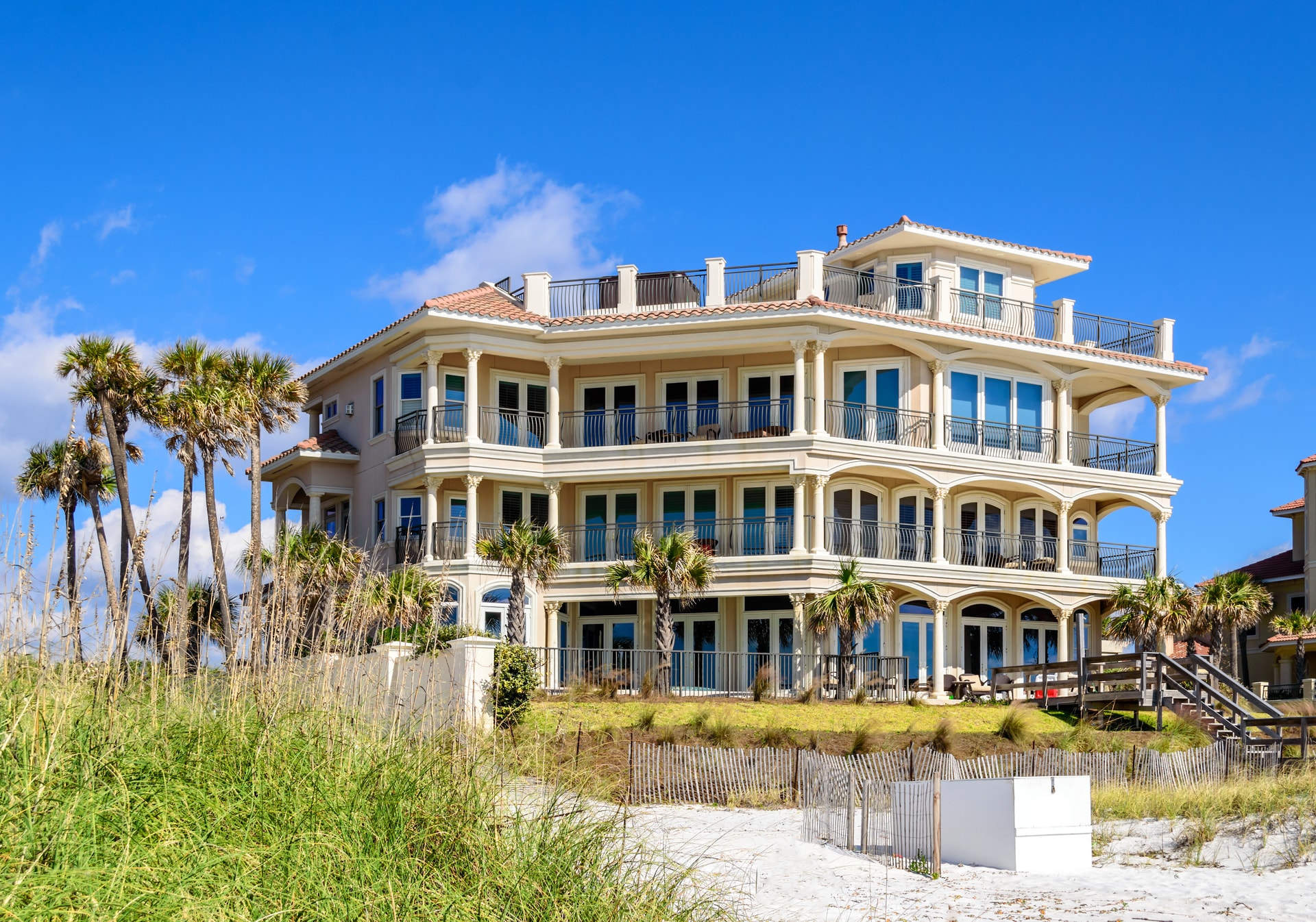 A large multi-storey beachfront home behind dunes and palm trees